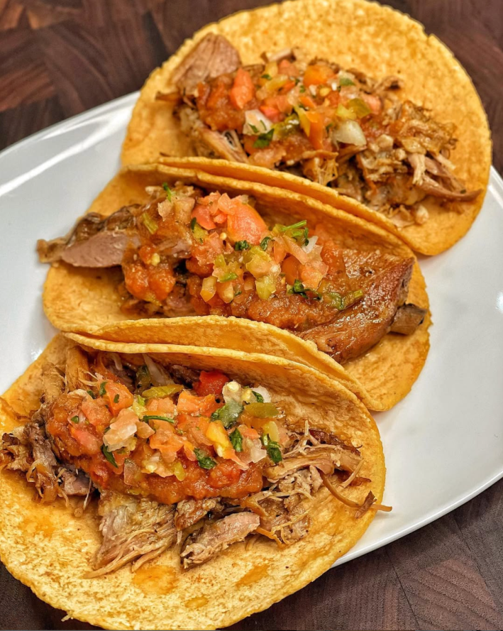 Three tacos de carnitas with pico salsa poured over it.