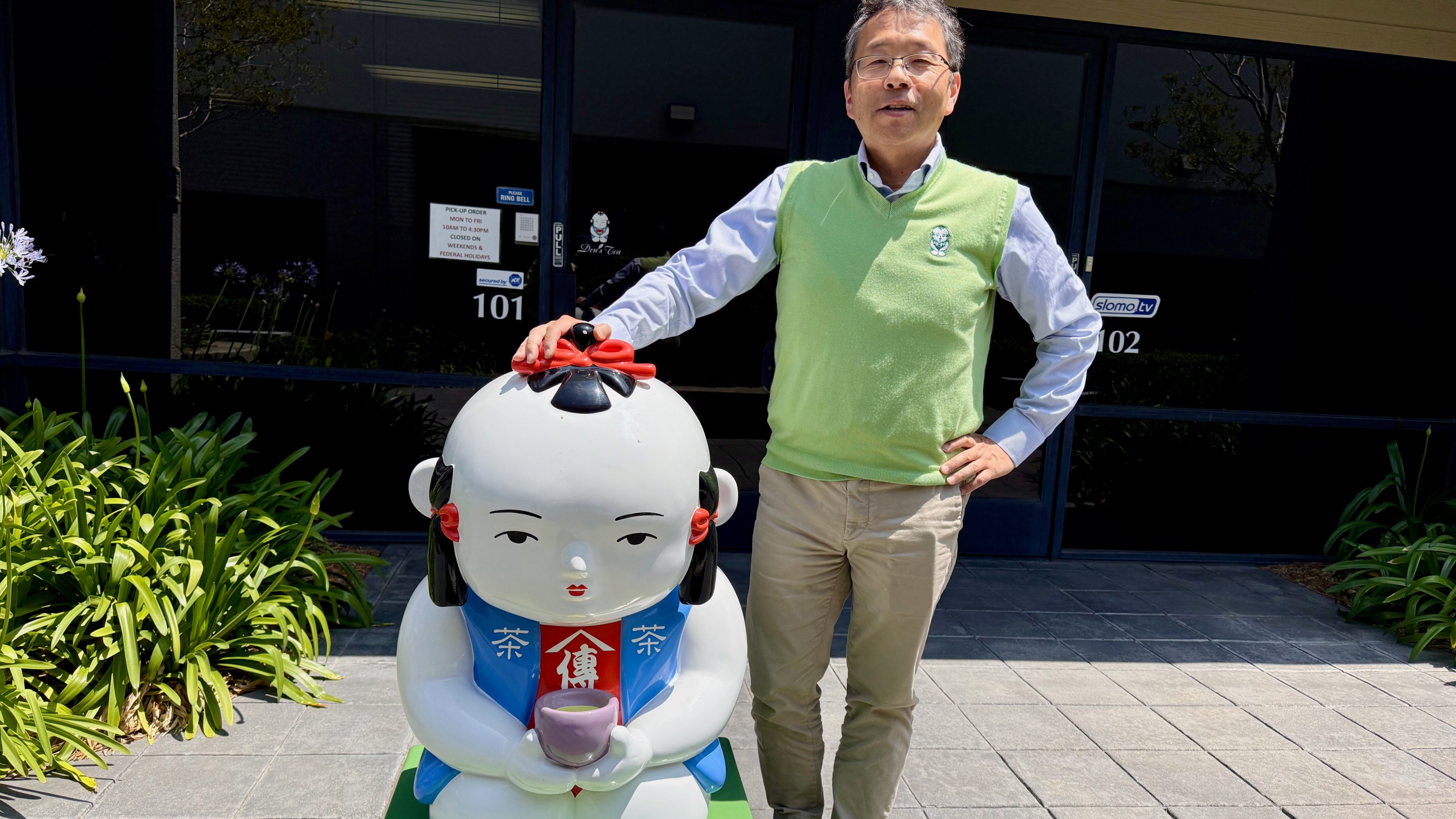 Den of Den's Tea posing next to their mascot.