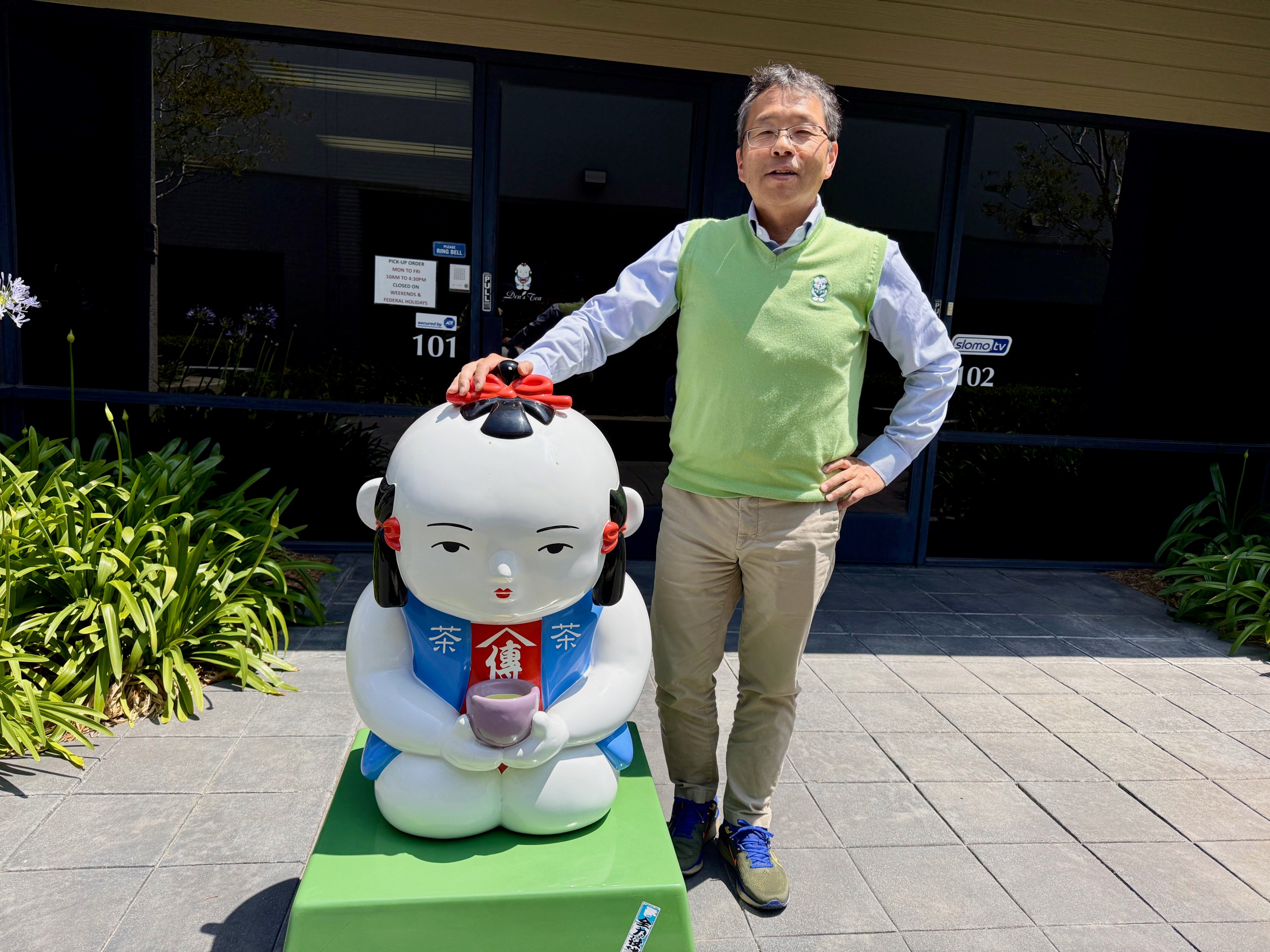 Den of Den's Tea posing next to their mascot.
